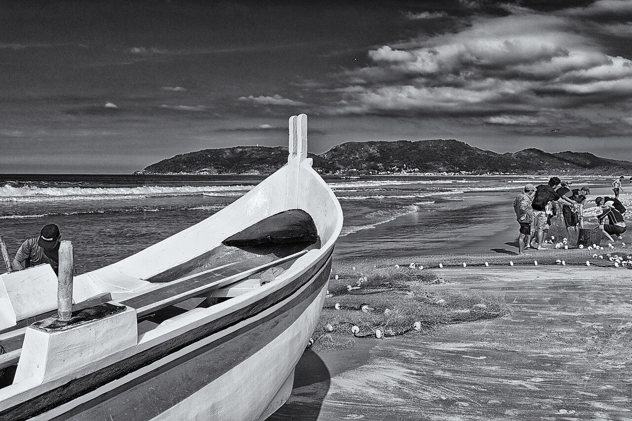A canoa do arrasto na areia, com a rede e os pescadores ao fundo
